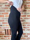 Person wearing black pants against a brick wall showing how the pants fold over