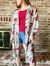 Woman wearing a patterned kimono over a red top and denim shorts against a brick wall.