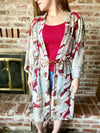 Woman wearing a patterned kimono over a red top in front of a brick wall.