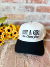 Trucker hat with 'Just a Girl Who Loves Jesus' text on a rustic surface with yellow flowers and brick wall background