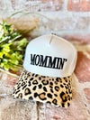 White cap with 'MOMMIN'' text and leopard print brim on a textured surface